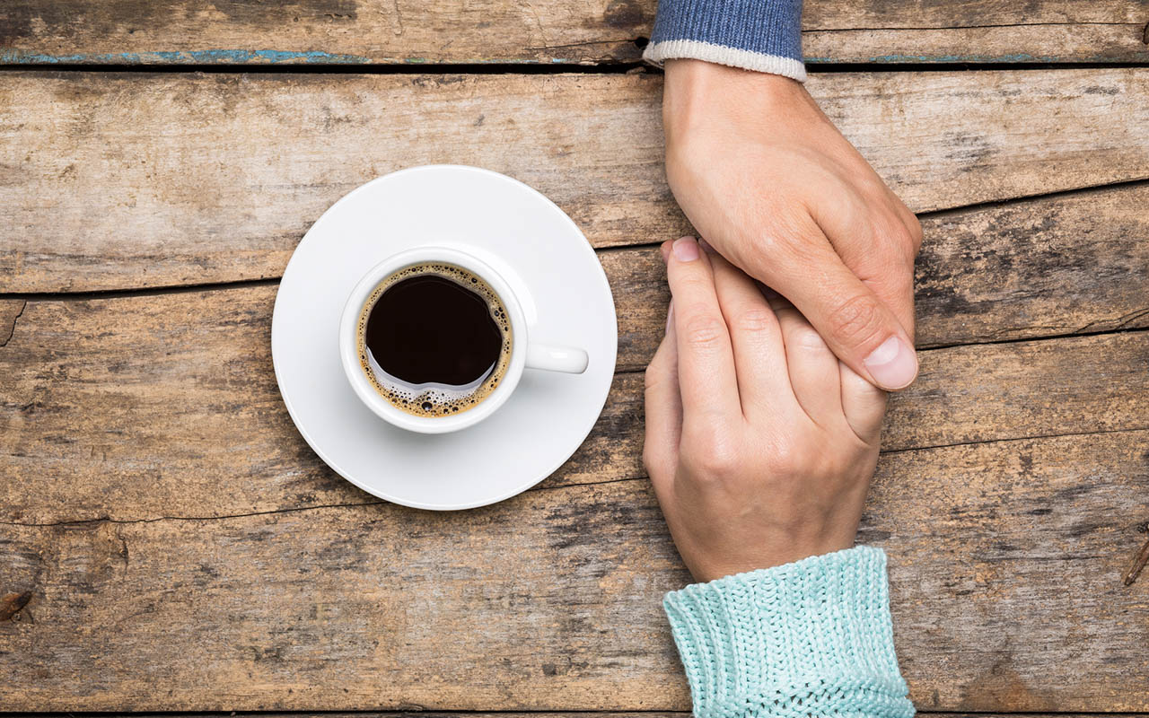 Man holds woman's hand with cup of coffee