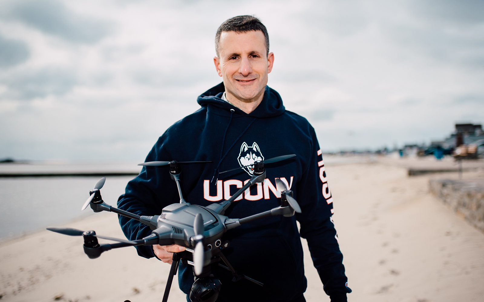 Jason Otrin poses on the beach with a drone in his hand.