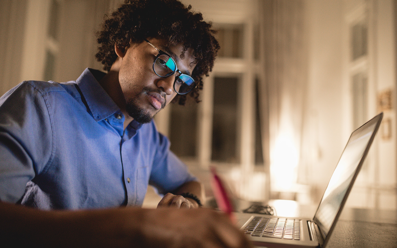 A black student studies at a laptop computer in a home office.