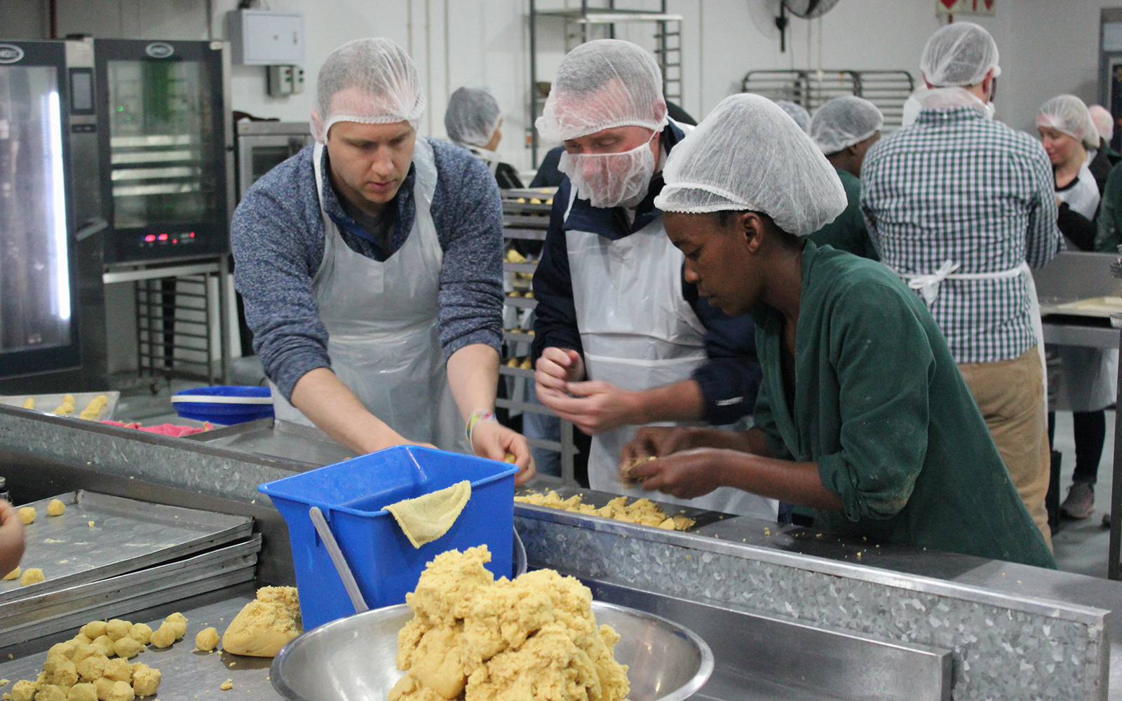 Rob Federici and Chuck Daly (EMBA ’20) working with local staff on the assembly floor at Khayelitsha Cookies in Cape Town.