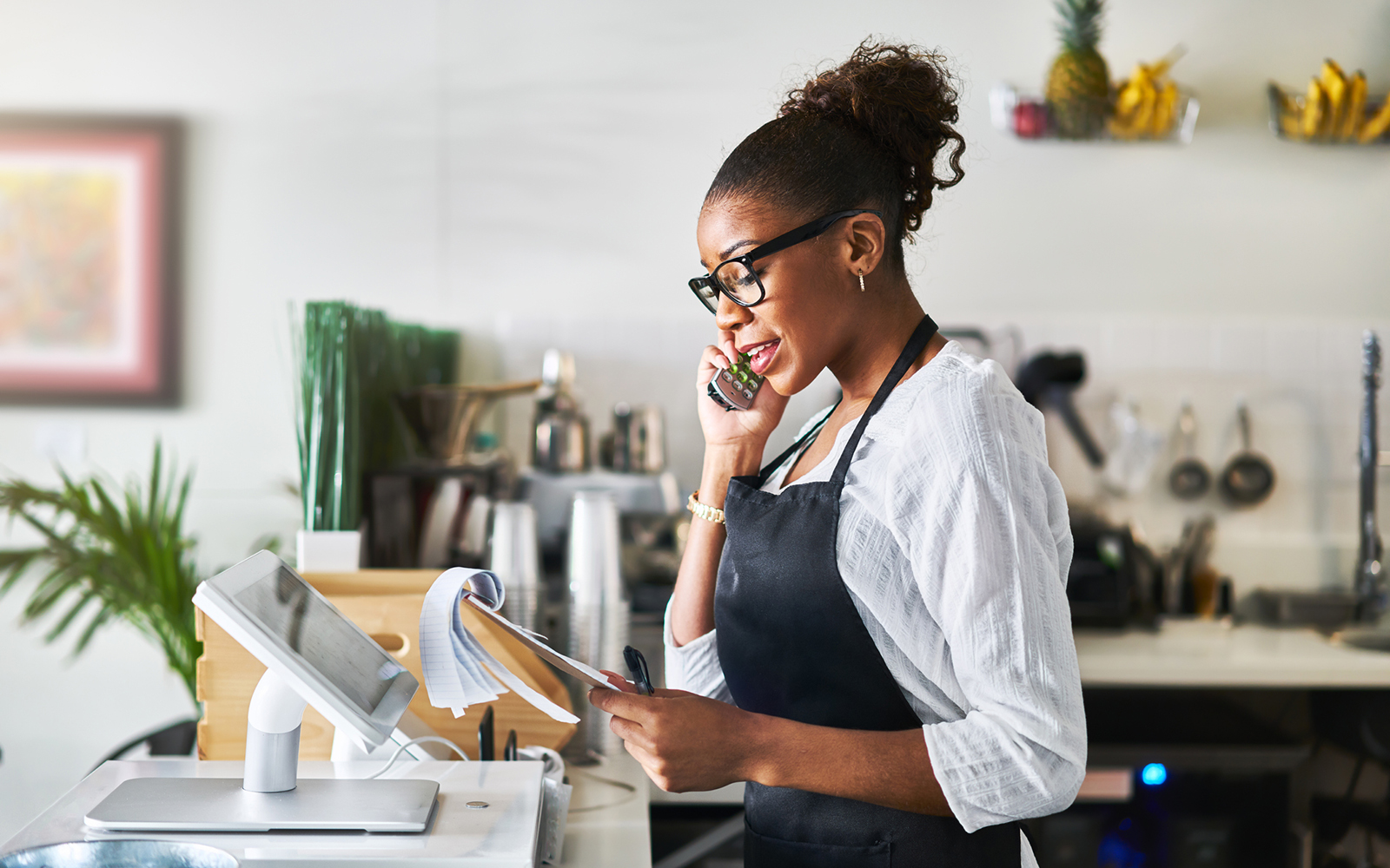 friendly woman taking order on phone at restaurant and writing on notepad during the day