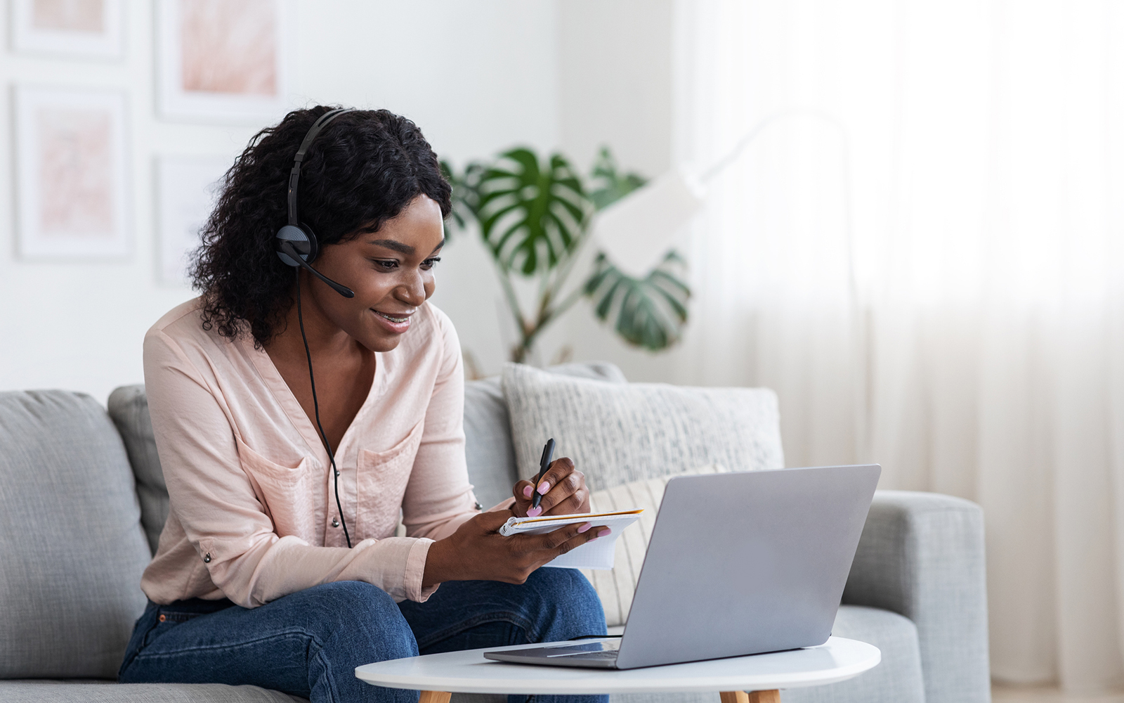 Online Education. Young Black Female Studying Online From Home With Laptop Computer And Headset And Taking Notes To Notepad, Enjoying Distance Learning, Watching Webinar In Internet, Copy Space