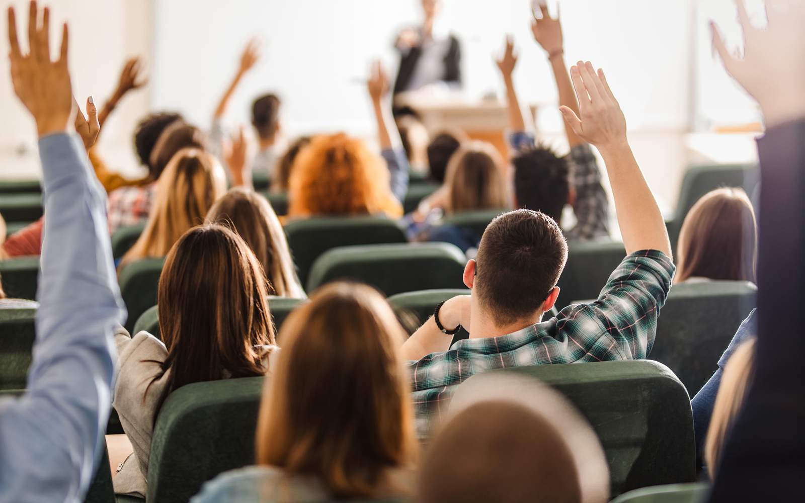 Back view of college students raising their arms on a class at lecture hall.