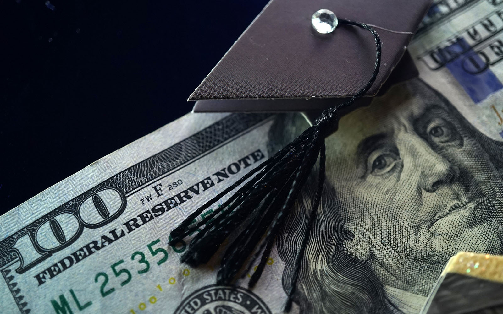 Image of a 100 dollar bill with a academic mortarboard positioned on Ben Franklin's head. 