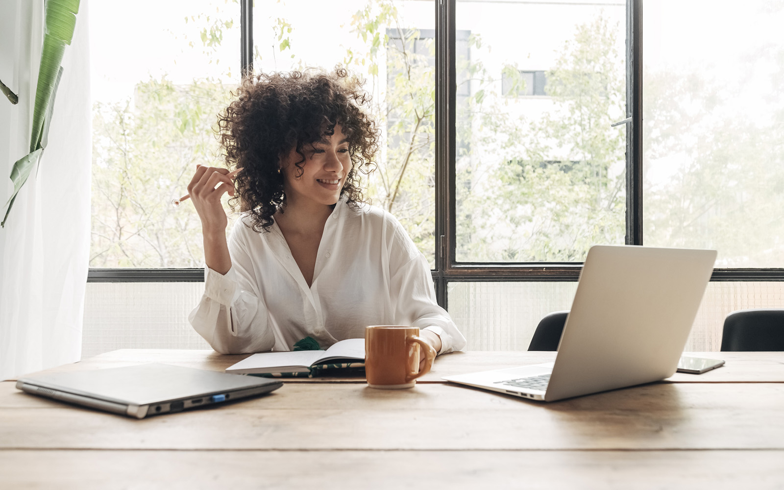 Smiling, happy, Young beautiful african american woman studying at home with laptop. Taking notes in notebook. Bright spacious living room. E-learning concept. Study at home concept.