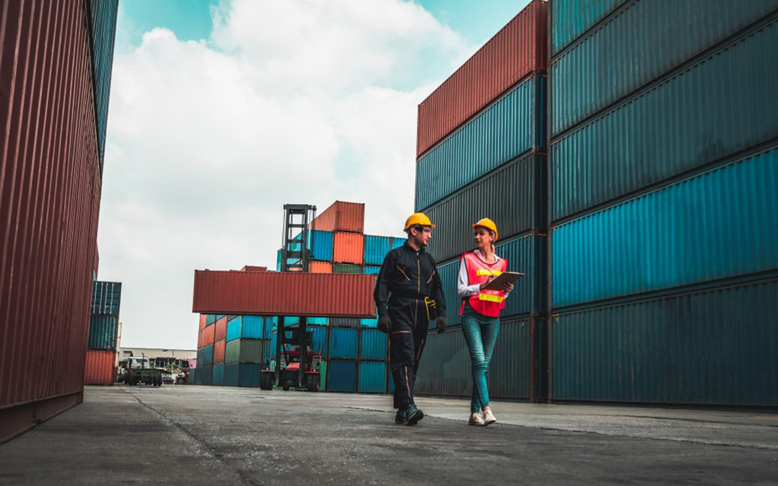 Two workers in hard hats walk side by side surrounded by shipping containers.